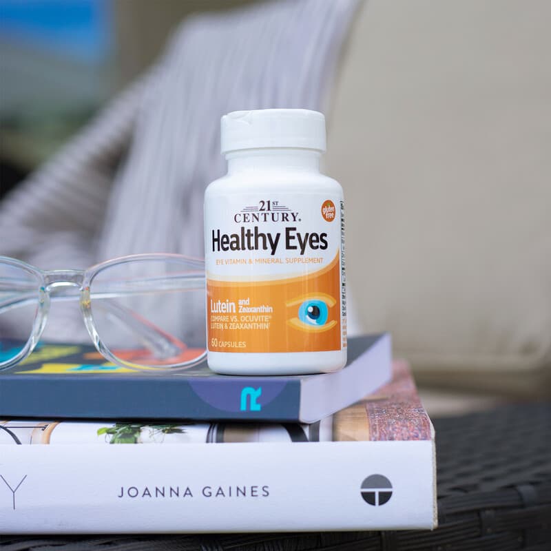 Bottle of 21st Century Healthy Eyes vitamins on a stack of books with glasses nearby.