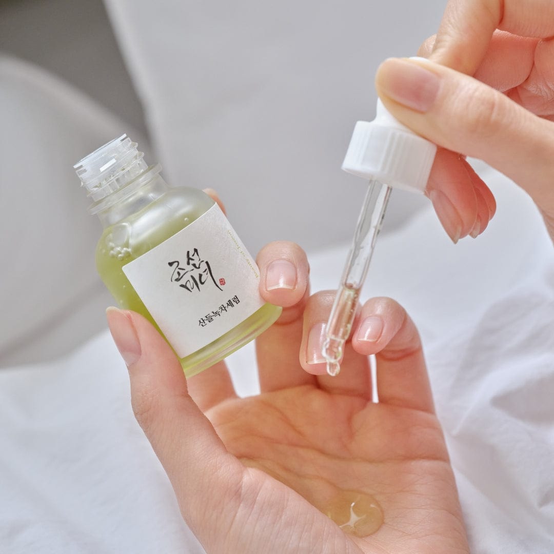 Hand holding a small bottle with a dropper, likely containing a skincare product.