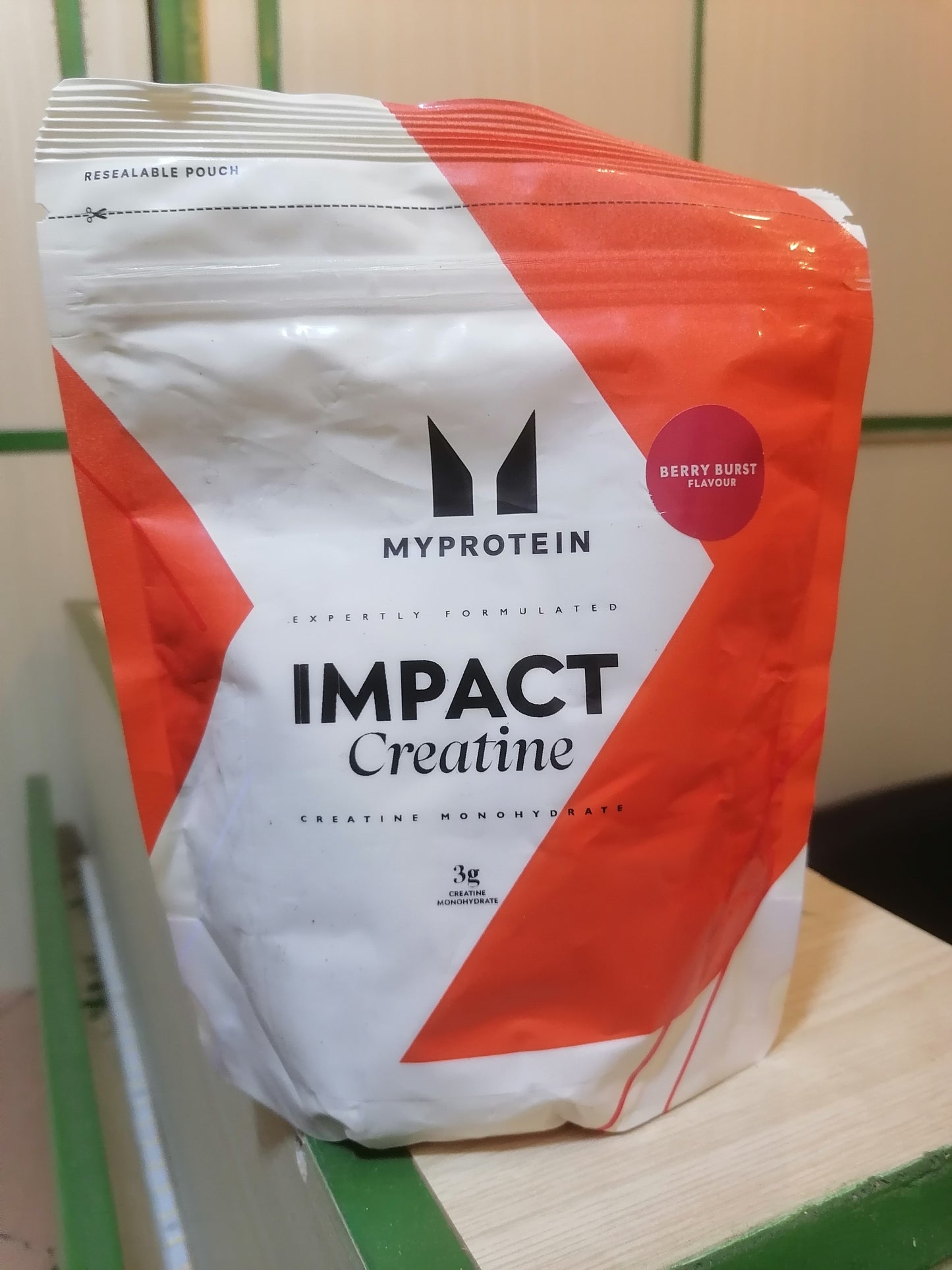 MyProtein Impact Creatine powder packaging on a wooden surface with a green background