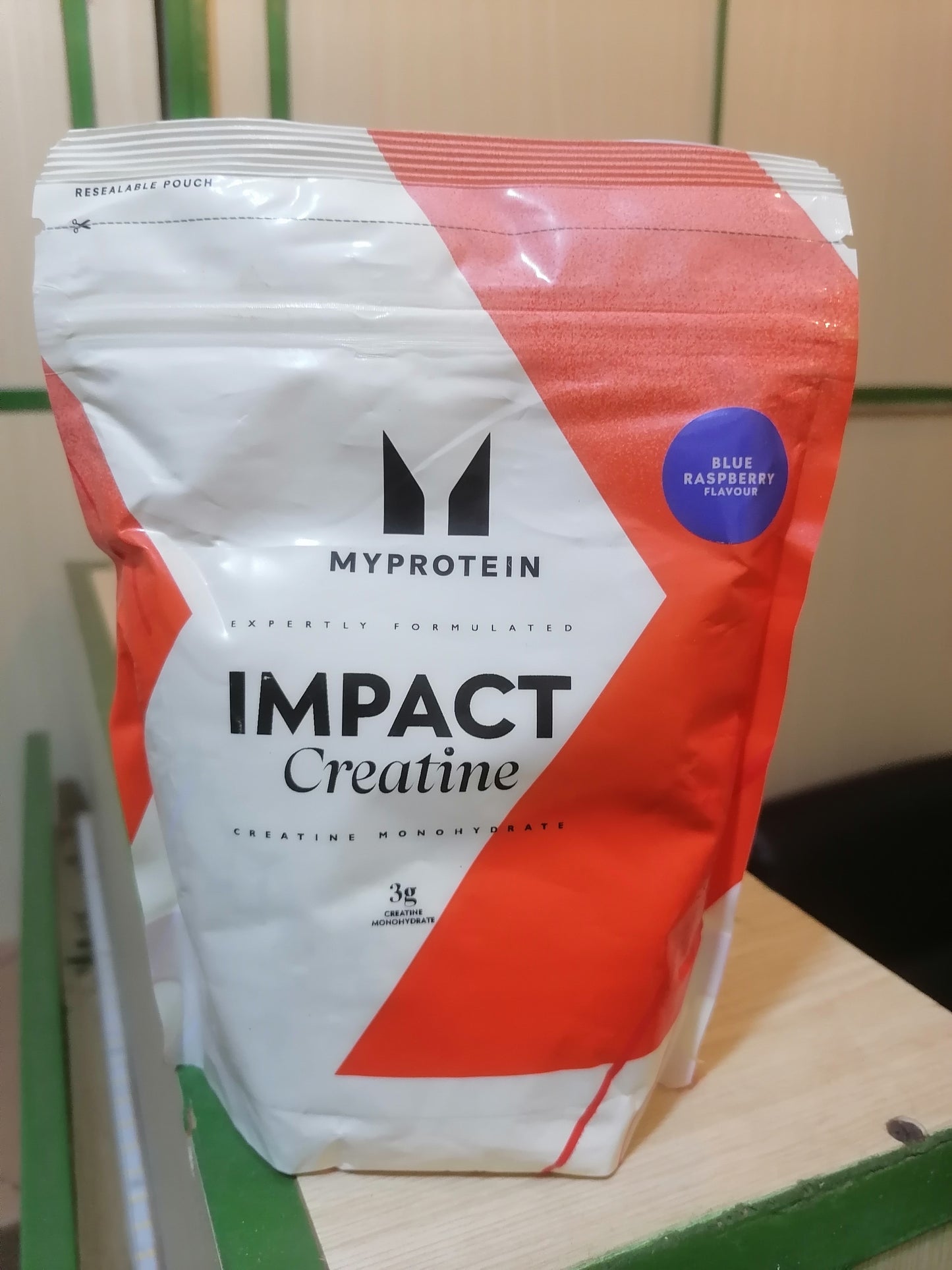 MyProtein Impact Creatine package on a wooden surface with a green background