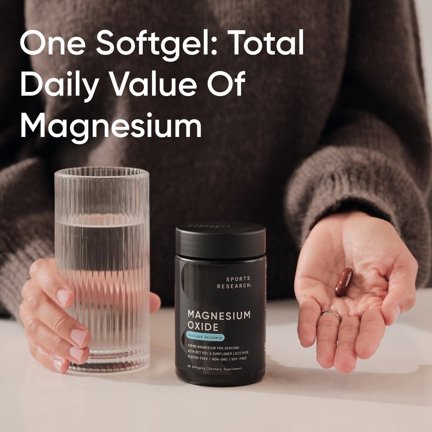 Person holding a supplement container, softgel, and glass of water with text about magnesium.